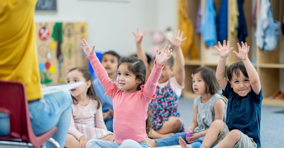 Preschool children sitting on the carpet with their hands in the air during circle time