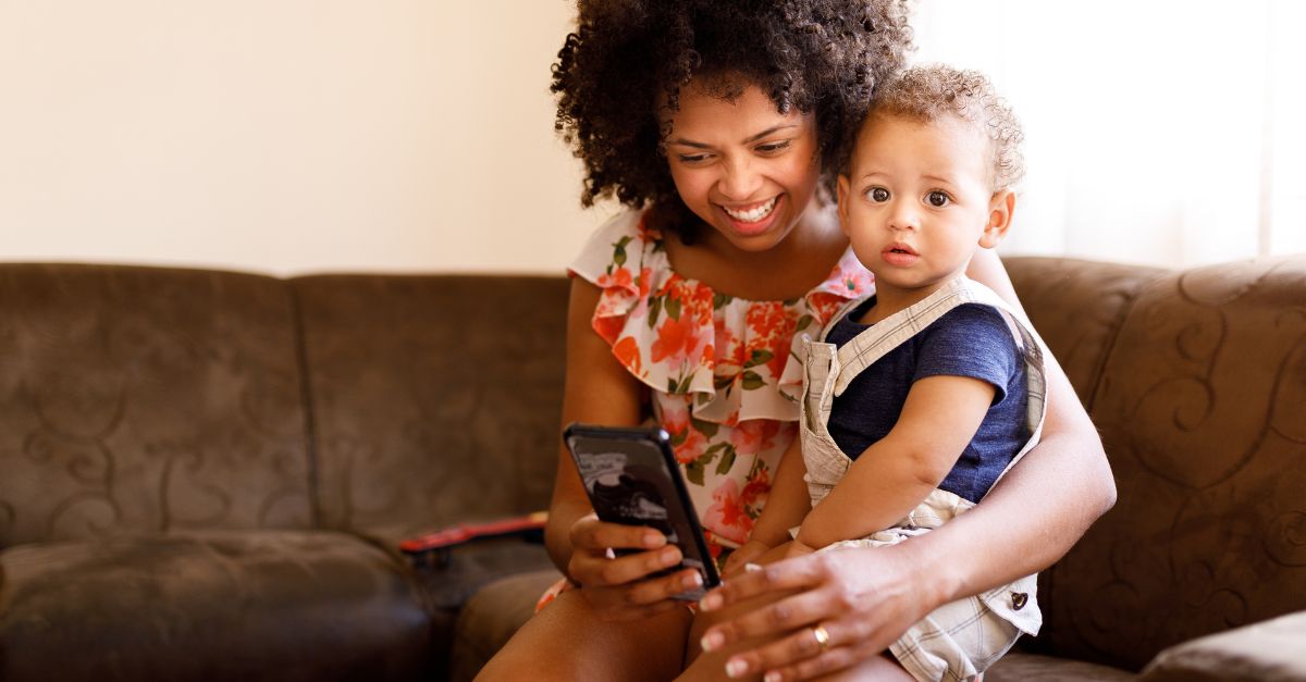 Mom holding her baby while smiling at her phone reading reviews of her childcare center