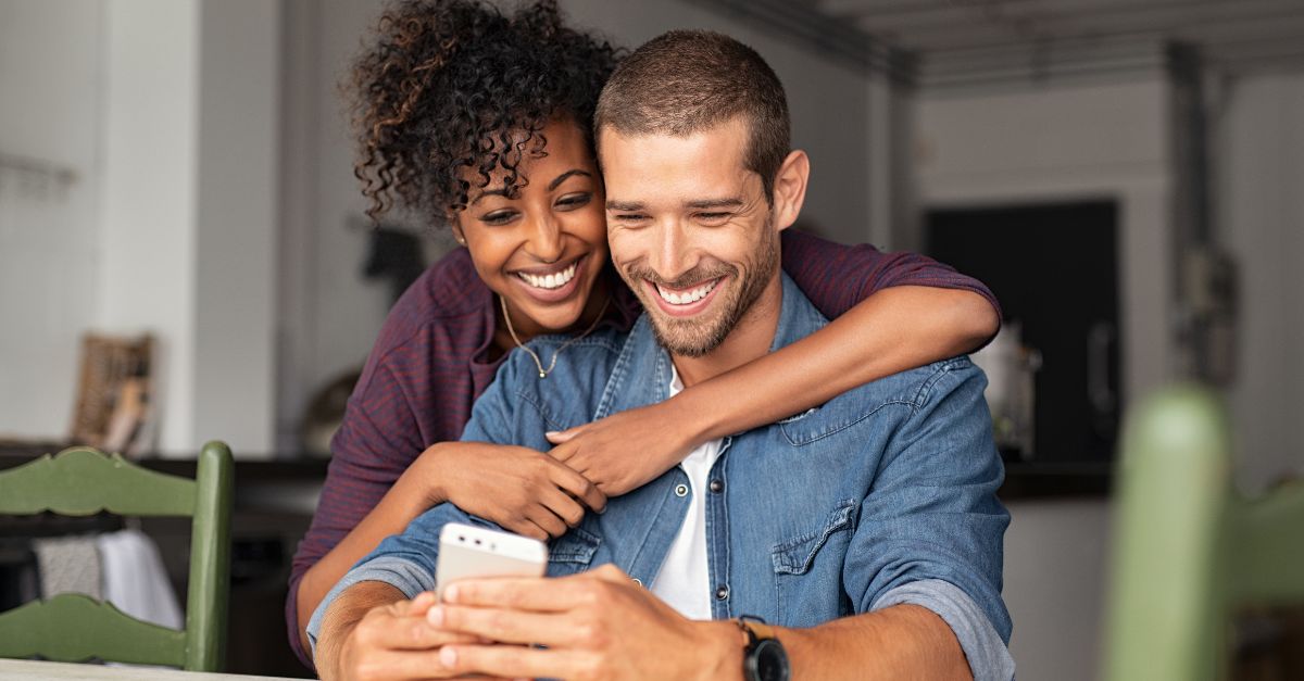 Parents smiling and looking at their phone as they get online updates from their child's daycare center