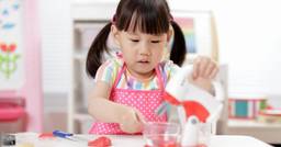 Little girl wearing an apron and focusing as she plays make-believe and pretends to bake with plastic baking utensils at preschool. 
