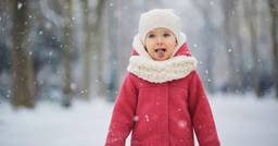 A preschool aged girl playing outside in the winter and catching snowflakes on her tongue. 