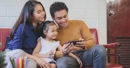 Two parents with their preschooler looking at a message from a daycare app highlighting what happened at daycare highlighting their family ties to their center