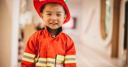 Little boy smiling at the camera as he dresses up as a firefighter at preschool. 