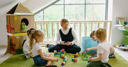 Home childcare provider sitting on the ground and engaging in play with  4 preschoolers