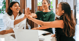 Three teachers sitting at a table and high-fiving