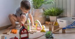 A preschool boy playing independently in a sunny corner of the classroom while building with wooden blocks and a train set