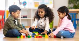 Three preschoolers engaging in play-based learning in the classroom and moving blocks around
