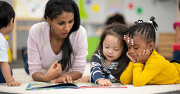 Group of preschoolers reading a book with their teacher