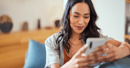 Childcare parent holding phone and smiling at updates from their childcare