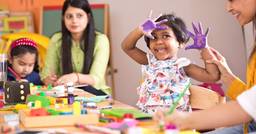Preschooler smiling at the camera while finger painting at school