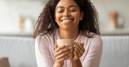 A home childcare provider holding a cup of coffee and smiling with their eyes closed. 