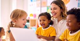 Center director smiling at a computer surrounded by kids because her center has long term financial stability