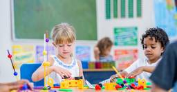 Two preschool children engaged in cognitive play with fine motor skill toys as they stack and construct items on the table. 