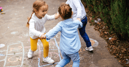 Three preschool girls holding hands and spinning in a circle outside