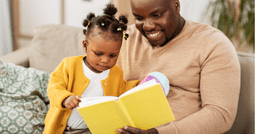 Dad and baby smiling and reading a book on the couch
