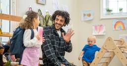 Early childhood educator waving and welcoming children into the classroom