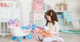 Little girl holding a baby doll and playing with pretend nursery items as she pretends to feed the baby and give them a bath in the preschool classroom. 