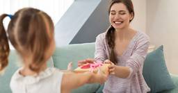 A young girl giving their early childhood educator a wrapped christmas gift. 