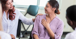 Teacher smiling and putting her hand on colleagues shoulder in sign of support during staff meeting