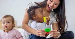Infant teacher smiling with two infants as they play with blocks