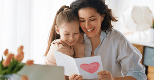 Mom and preschool daughter hugging, looking at mothers day card made at daycare. 