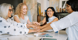 Four early childhood professionals sitting at a table, all hands in the middle, smiling 