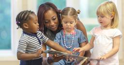 Early childhood educator sitting with three toddlers reading