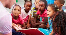 Group of daycare children sitting and listening to their teacher read them a story developing their emotional vocabulary.