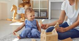 Toddler and teacher playing with wooden house and dolls at school