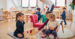 Three preschool and kindergarten aged children playing together with blocks and wooden toys in the classroom. 