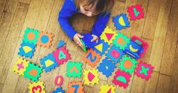 A preschool child playing with large foam numbered puzzle pieces on the floor as they engage develop their cognitive skills