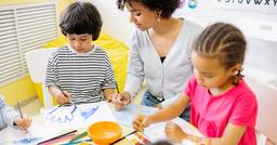 Preschool teacher helping two preschoolers complete a process art activity in a classroom.