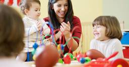 A preschool teacher clapping and smiling as she praises the young children at her table who just accomplished their tasks. 