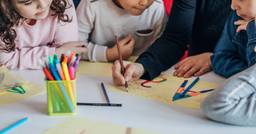 Three children sitting with their preschool teacher as they practice drawing uppercase and lowercase letters. 
