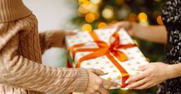 A wrapped christmas gift being exchanged between the hands of an early childhood educator and a parent. 