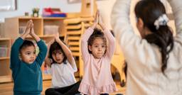 Kindergarten teacher leading three children in yoga poses
