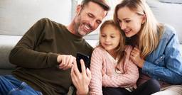 Parents and preschooler sitting together looking at daily report updates on their phone and smiling