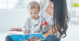 Infant educator with an infant sitting in her lap while they read a book 