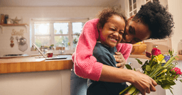 Mom hugging her preschool daughter and smiling as she holds her bouquet of flowers on mothers day. 