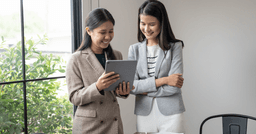 Two early childhood educators smiling and reviewing their daily documentation on an Ipad