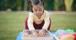 Toddler outside in spring engaging in sensory play using a sensory bin