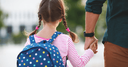 A father and daughter from the back as they walk towards school for morning drop off