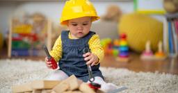 Toddler wearing construction helmet and playing with pretend construction tools