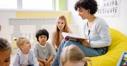 Group of preschoolers sitting and watching their teacher read to them during a structured reading time. 