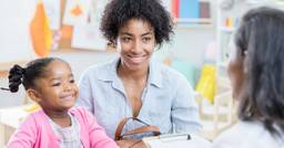 A mom and daughter smiling as they look at their preschool teacher during a family meeting