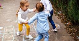 Three preschoolers holding hands and playing outside
