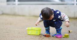 Toddler looking down and exploring mud in the outdoor playground 