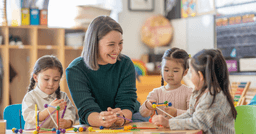 Preschool teacher sitting at a table smiling with three children
