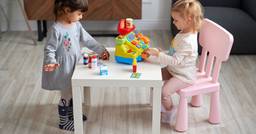 Two preschool children engaged in pretend play in their early childhood classroom. One sitting behind the cash register and the other placing pretend pharmacy items on the table.