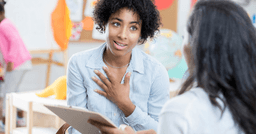Preschool teacher with hand on chest in conversation with parent